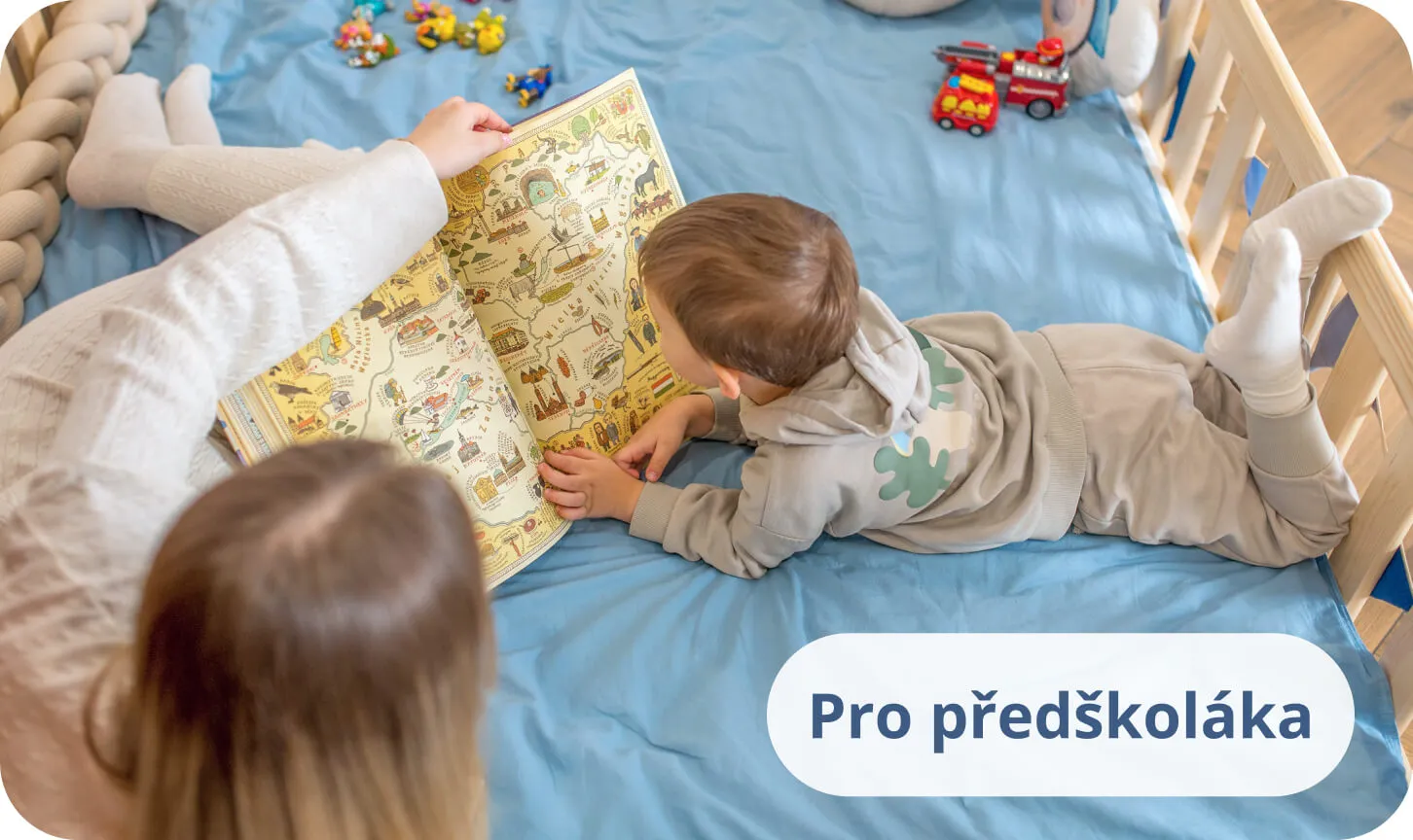 Malý chlapec s maminkou čtoucí barevnou knihu na modrém povlečení v borovicové posteli.